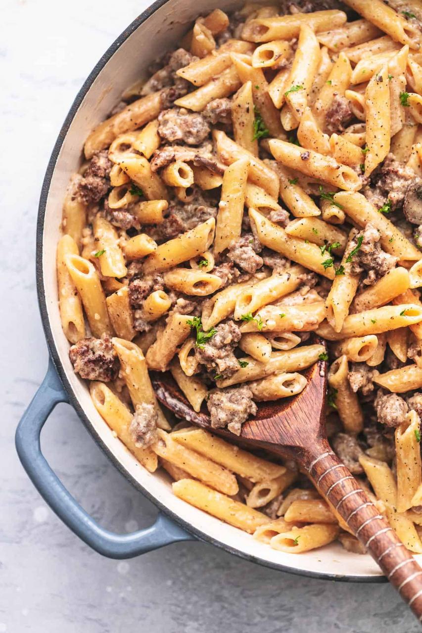 Nudeln mit Wurst und Penne-Nudeln in einer Pfanne mit einem Holzlöffel